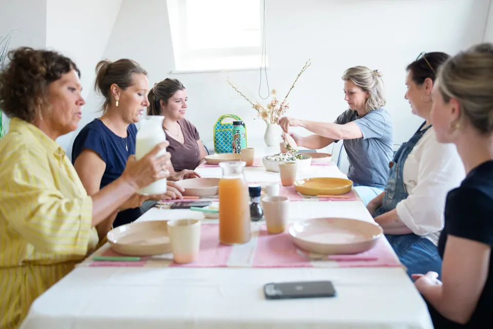 Deelnemers lunchen samen aan tafel in het atelier