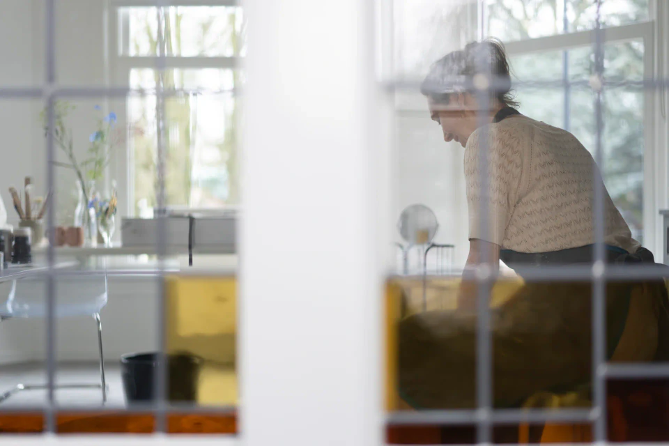 Siep werkt in haar lichte atelier, gezien door het glas-in-loodraam