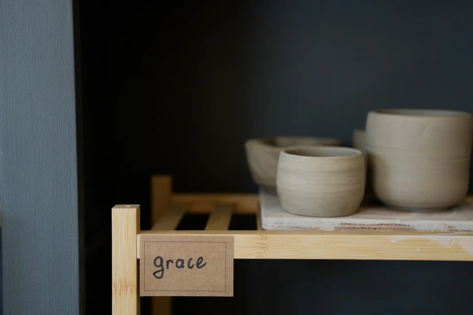 Zelfgedraaide kommen en bekers op een plank in het atelier